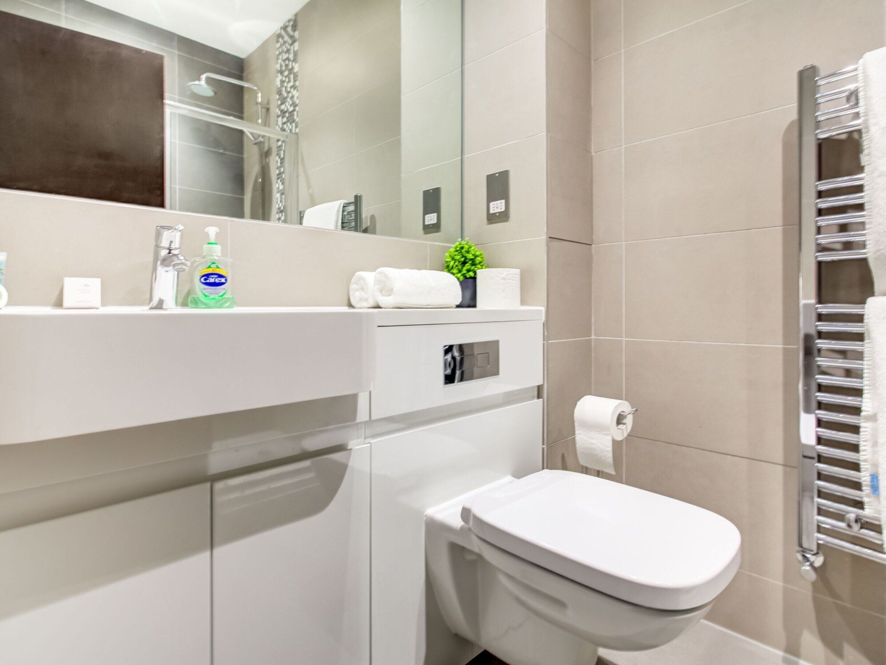 A modern bathroom with a toilet, a sink with a mirror, and a towel rack.