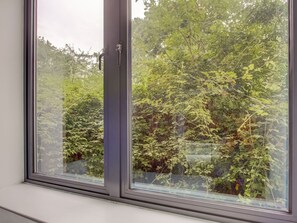 A window with a view of dense green foliage outside. - Simplistic Apartment in Milton Keynes near Willen Lake (Milton Keynes)