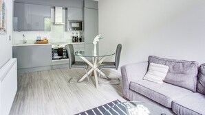 A modern kitchen with grey cabinets, a glass dining table, and a grey sofa. - Simplistic Apartment in Milton Keynes near Willen Lake (Milton Keynes)