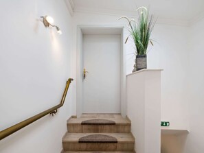 Una escalera con barandilla de latón, una planta en maceta en el descansillo y una puerta blanca al final.