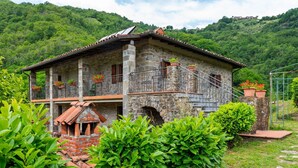 A stone building with a tiled roof, a balcony with potted plants, and a brick chimney.