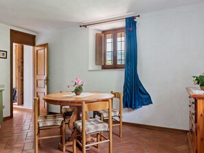 A dining area with a wooden table and chairs, a window with blue curtains, and a door leading to another room. - Belvilla by OYO La Casa sul Fiume 3 (Fosciandora)