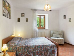 A bedroom with a bed, a chair, a window with a view, and a lamp. - Belvilla by OYO La Casa sul Fiume 3 (Fosciandora)
