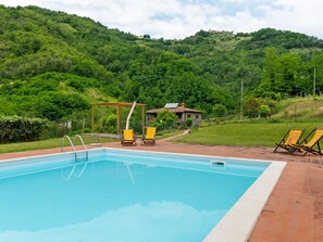 A swimming pool with two lounge chairs, a pergola, and a stone building in a lush green landscape. - Belvilla by OYO La Casa sul Fiume 3 (Fosciandora)