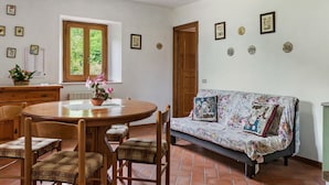 Un comedor con una mesa redonda de madera, cuatro sillas, un sofá con tapicería floral y una ventana que ofrece vistas al verdor.