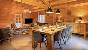 A wooden interior with a large dining table, chairs, a fireplace, and a kitchen area. - Elegant Chalet in Manhay With Sauna (Manhay)