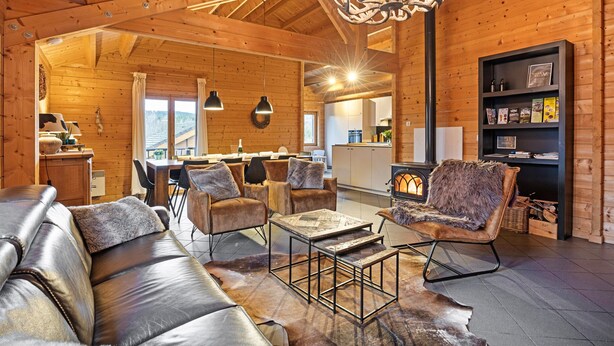 A cozy log cabin interior with leather sofas, a fireplace, and a dining area. - Elegant Chalet in Manhay With Sauna (Manhay)