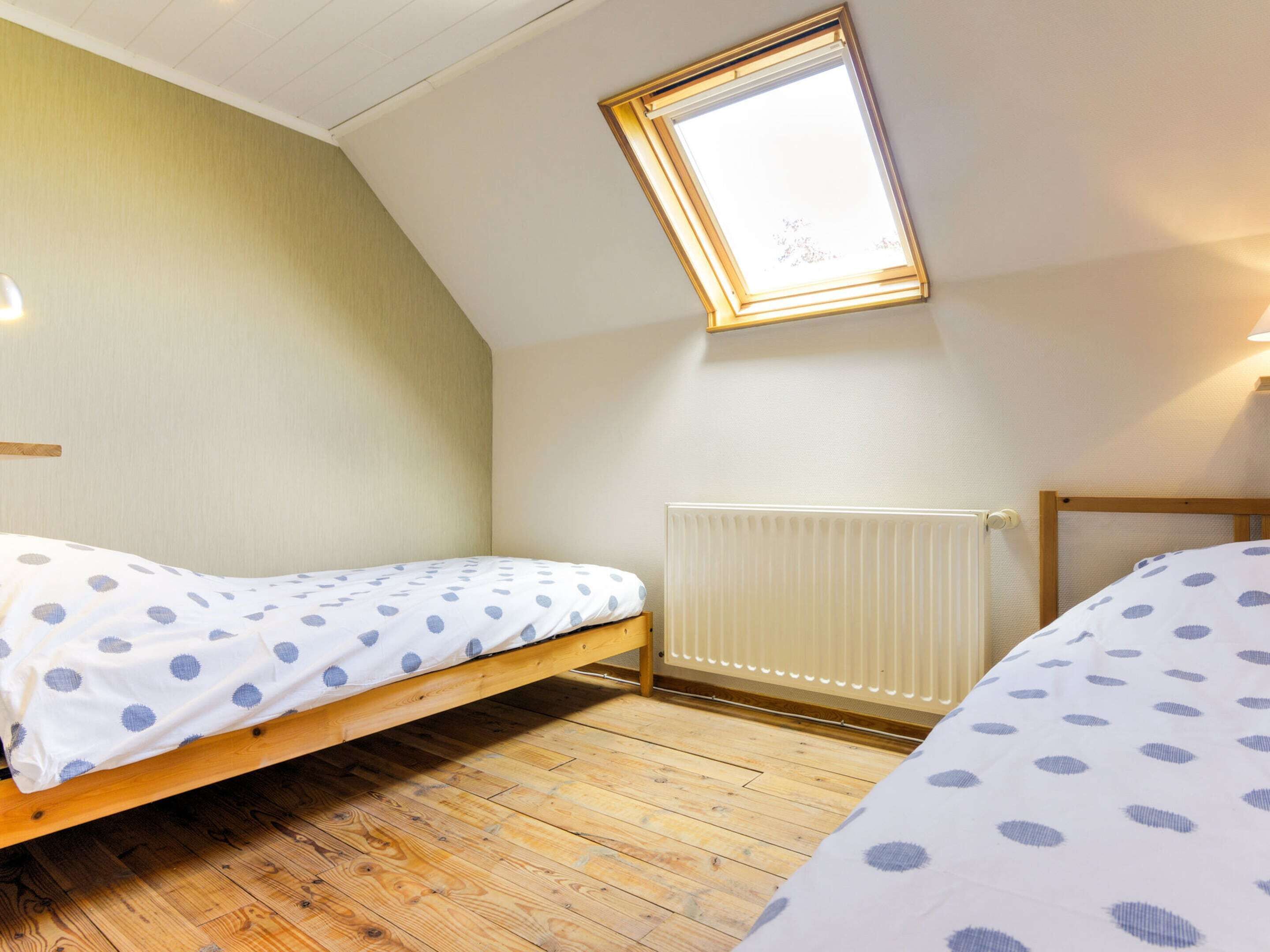 A small, single-room apartment with a sloped ceiling, a skylight, a radiator, and two beds with polka dot bedding.