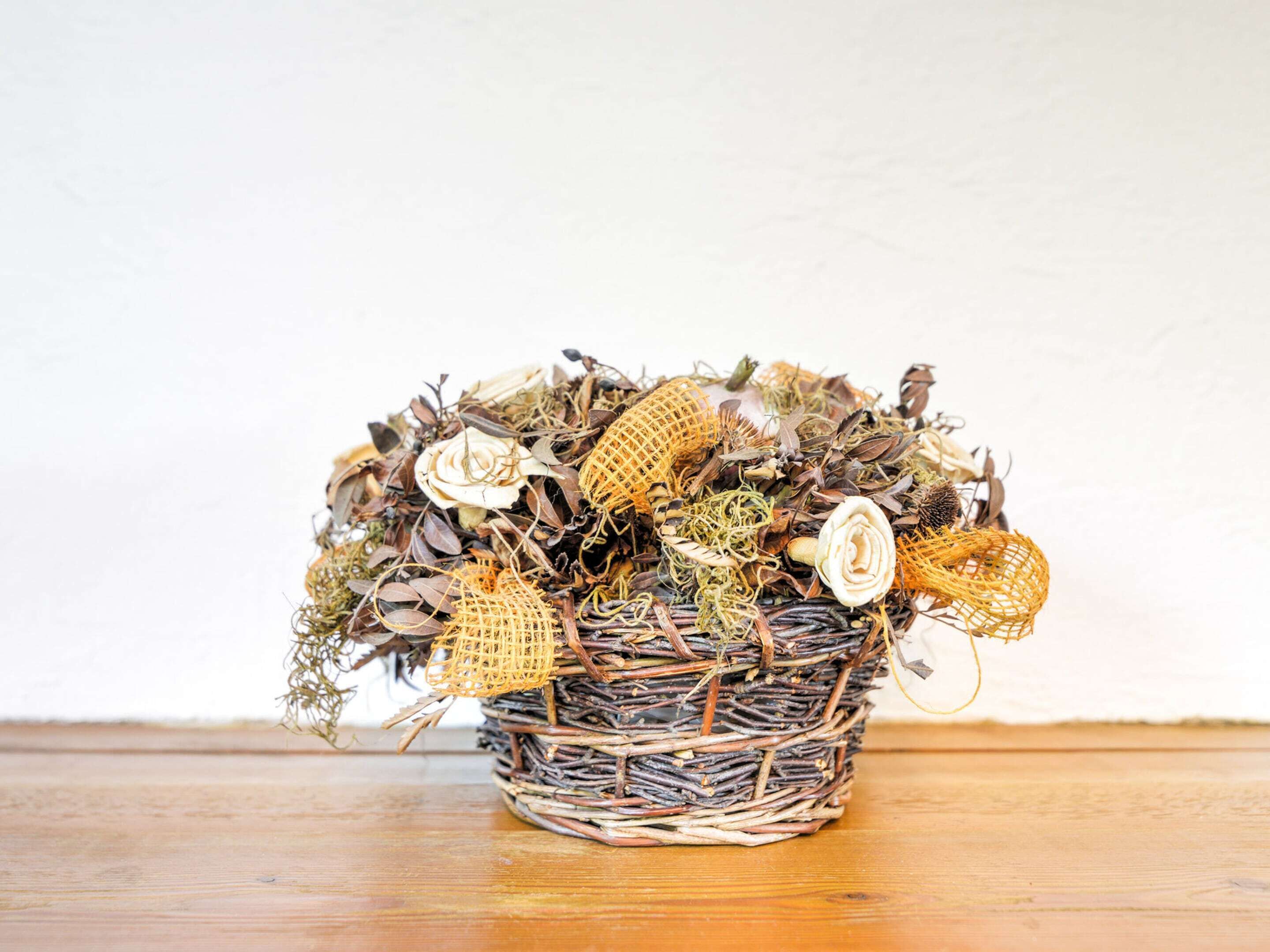 Ein Korbbusch mit getrockneten Blumen und Blättern auf einer Holztischplatte.