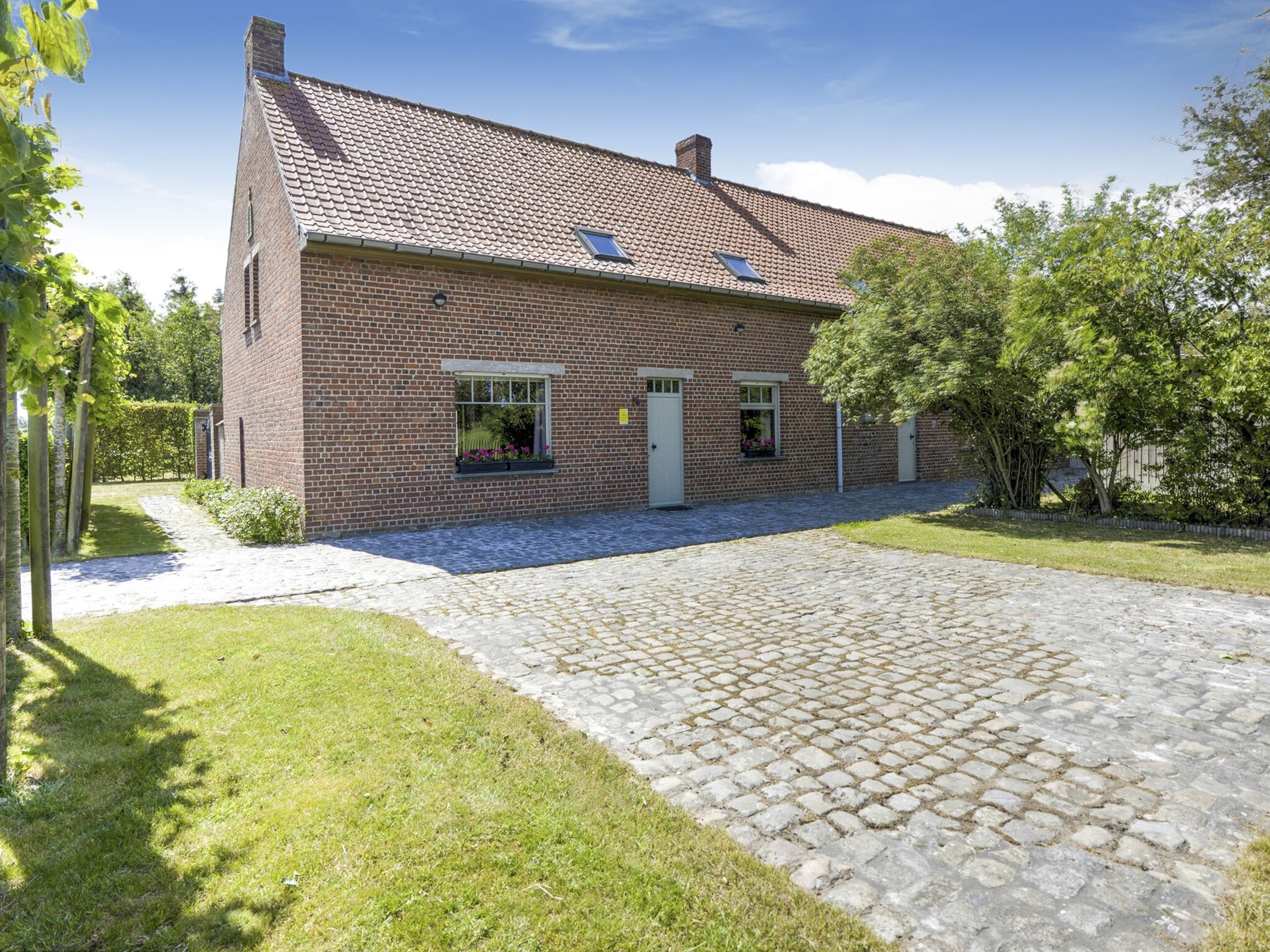 A brick house with a tiled roof, a paved driveway, and a small garden area.