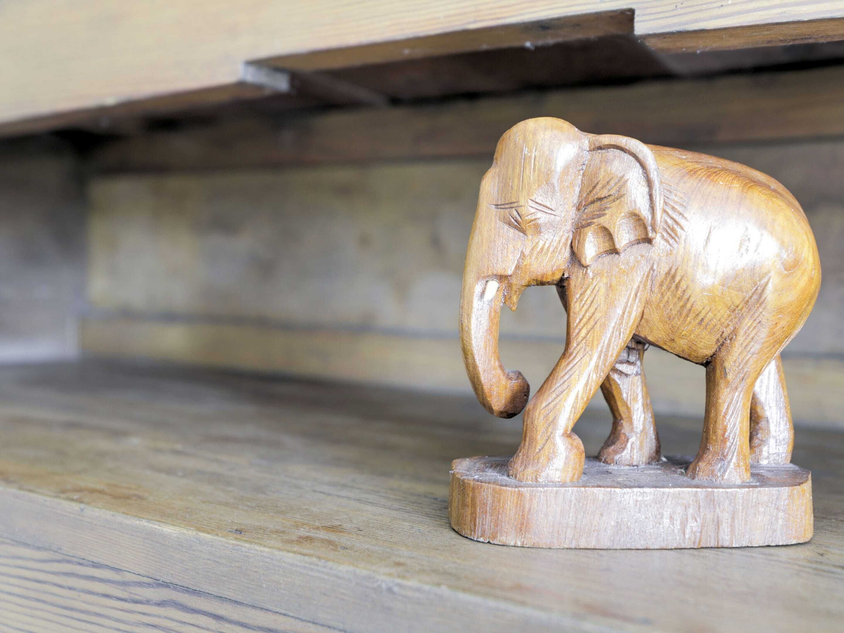 Une sculpture d’éléphant en bois, posée sur une plateforme en bois.