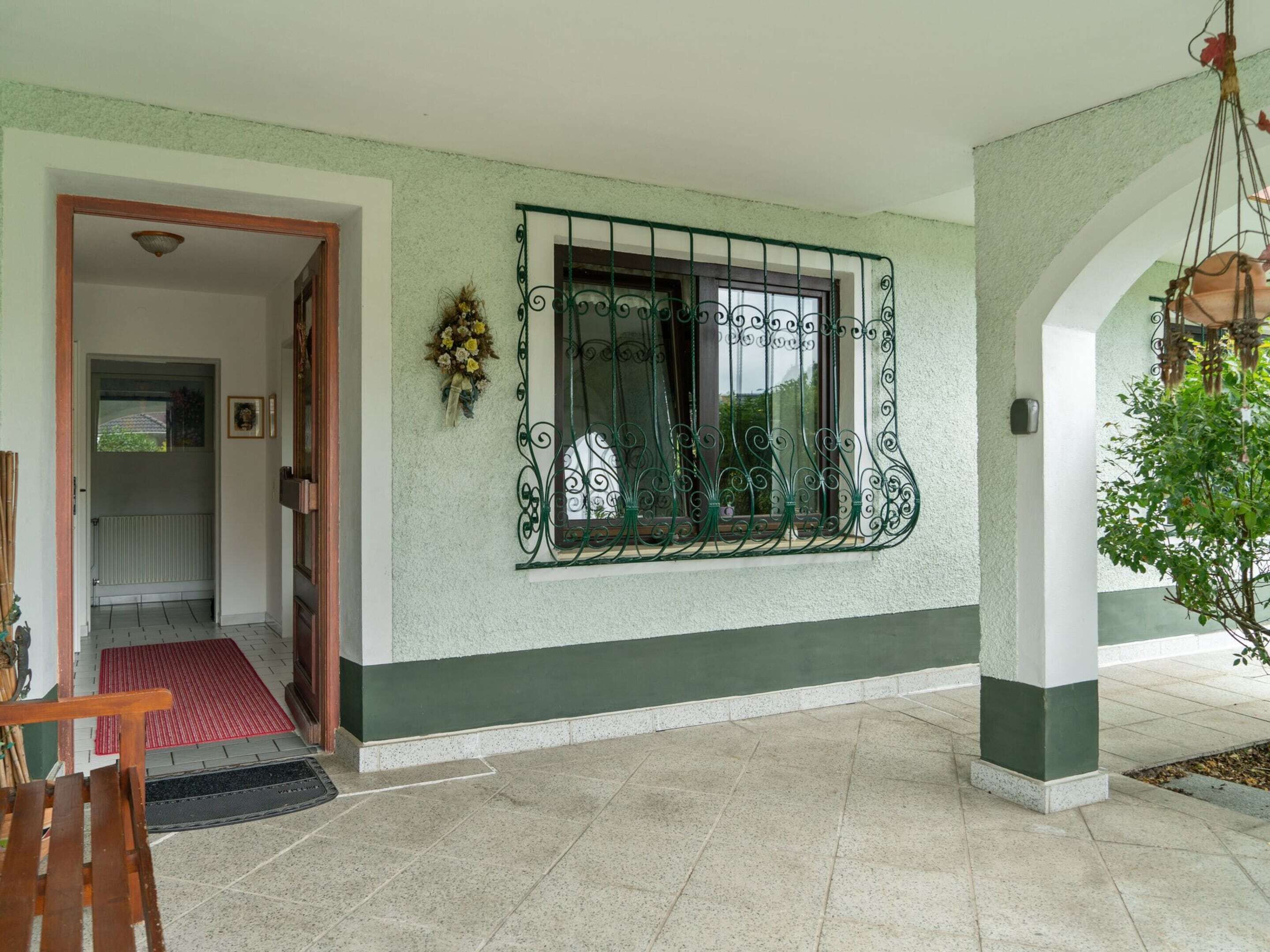 A clean, well-maintained entrance with a tiled floor, a red mat, and a wooden bench.