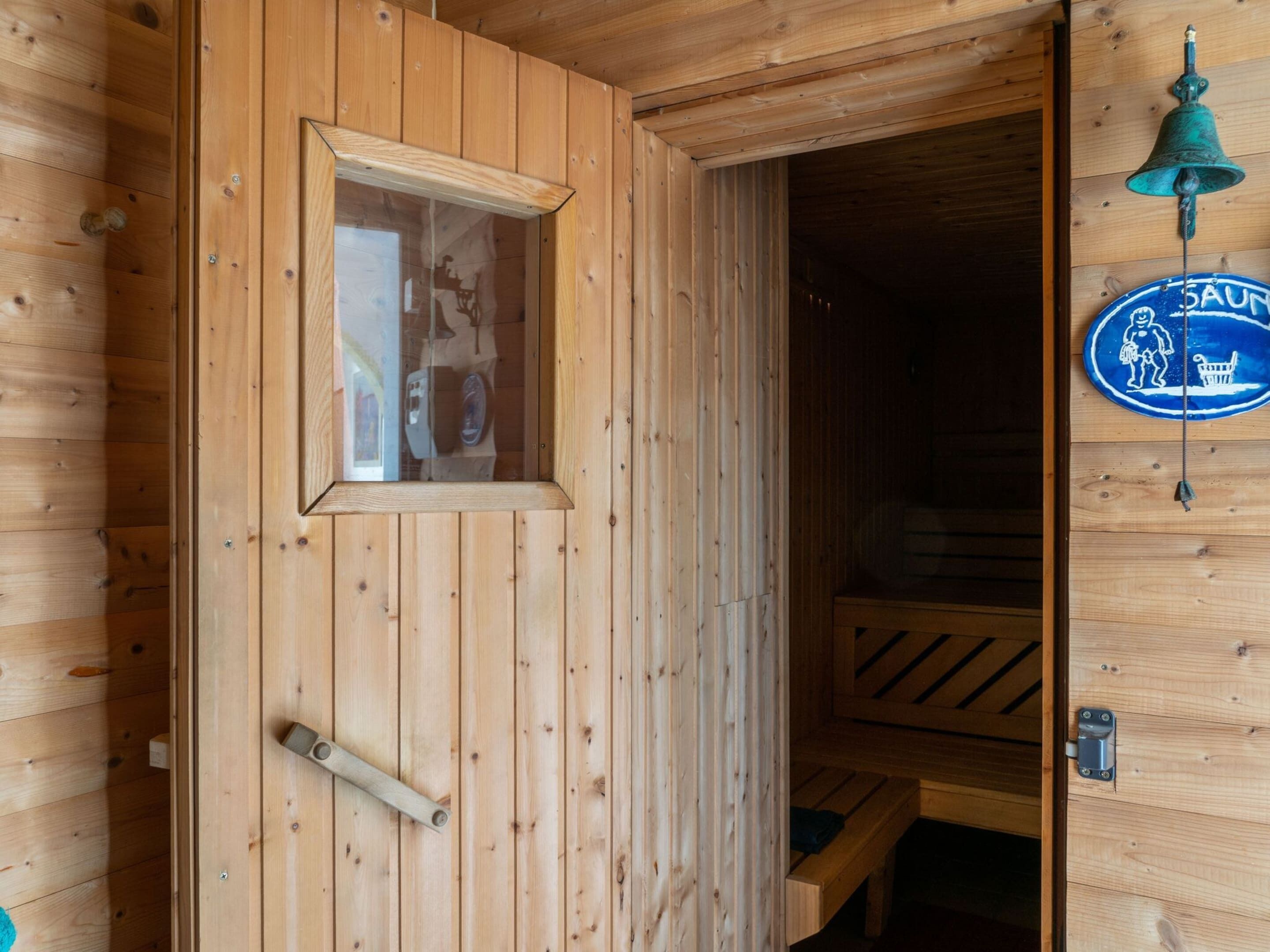 A wooden sauna room with a bench, a window, and a bell.