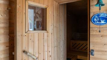 A wooden sauna room with a bench, a window, and a bell.