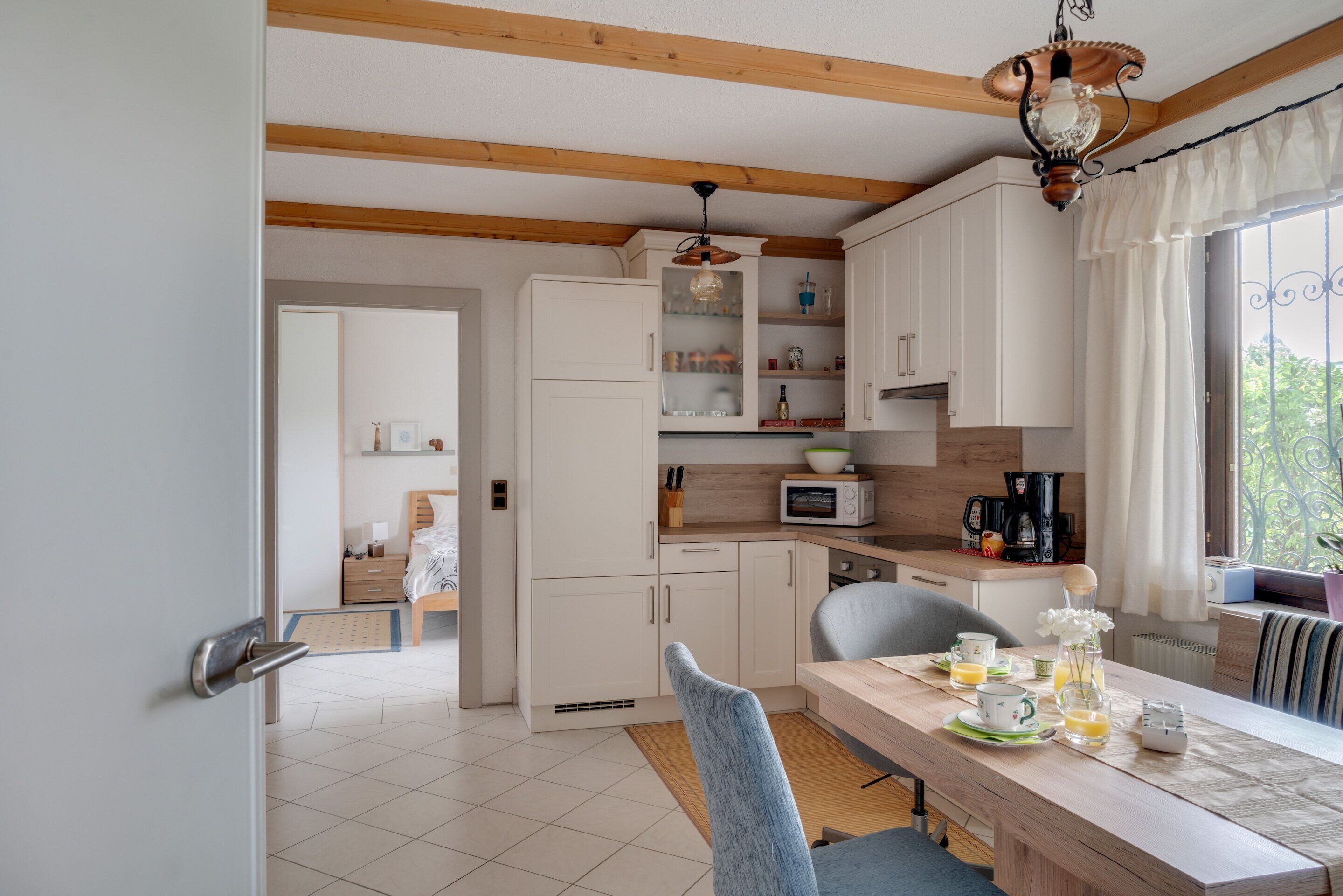 Een moderne keuken met witte kastjes, een ontbijt aan tafel gedekt, en uitzicht op het groen door een raam.