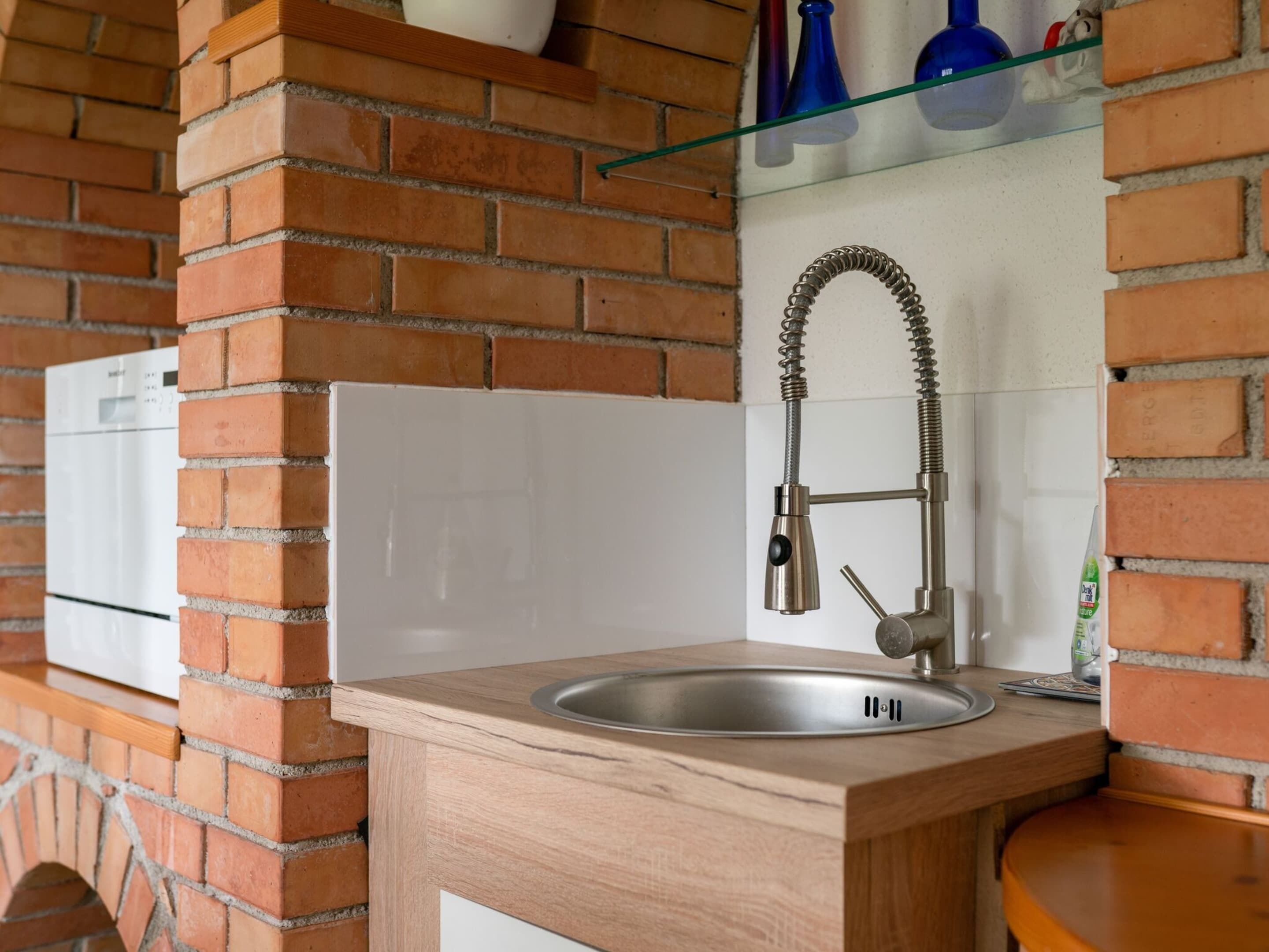 A kitchen with a stainless steel sink, a wooden countertop, and a brick wall.