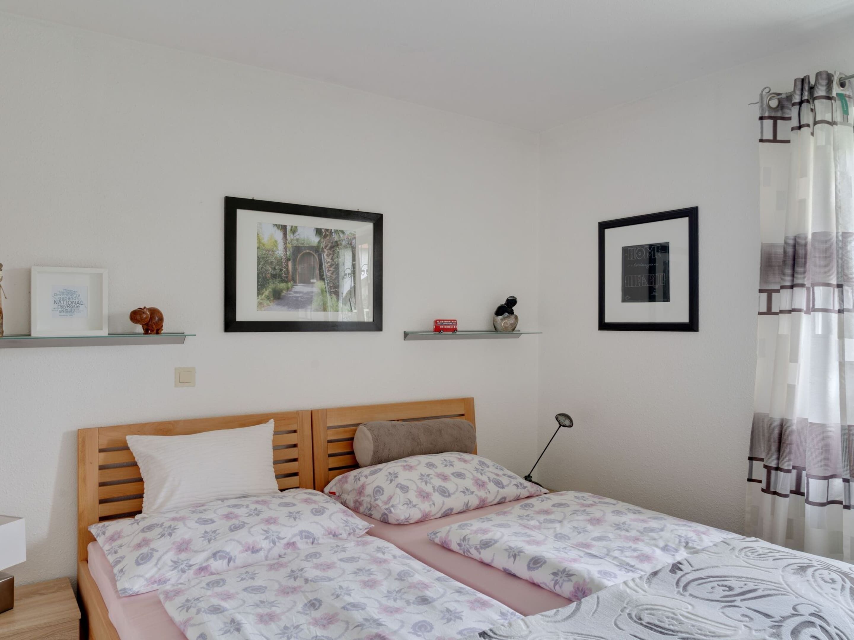 A bedroom with a wooden bed, two framed pictures on the wall, and a bedside table.