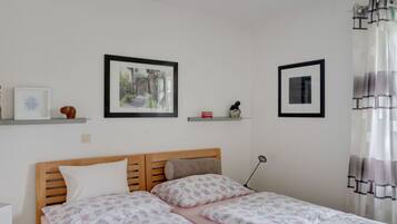 A bedroom with a wooden bed, two framed pictures on the wall, and a bedside table.