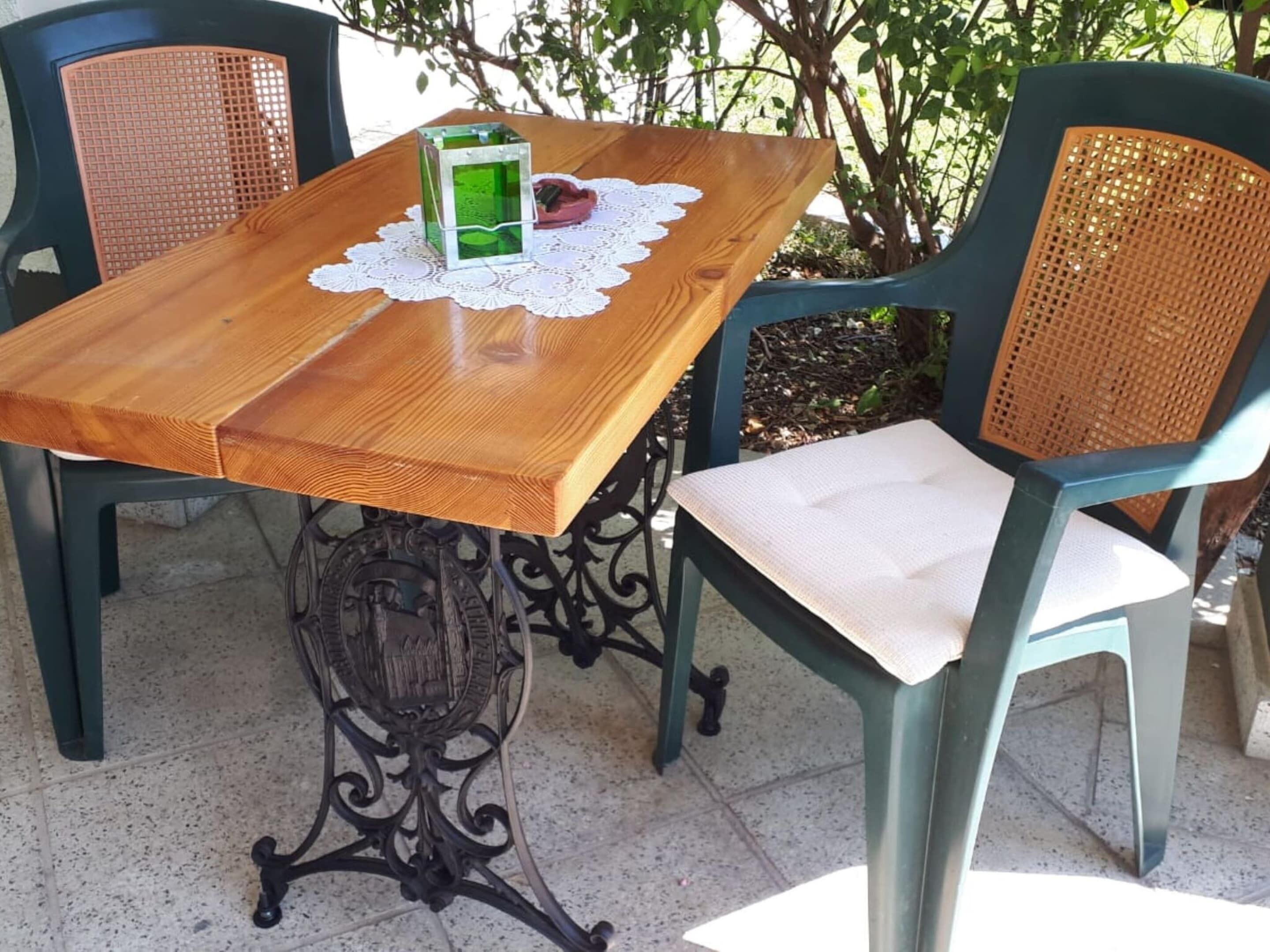 Un tavolo in legno con un sottobicchiere in pizzo, un candelabro in vetro verde e un posacenere rosso. Due sedie in vimini con sedili imbottiti sono disposte attorno al tavolo.
