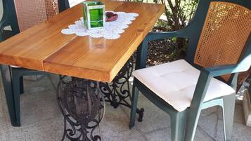 Un tavolo in legno con un sottobicchiere in pizzo, un candelabro in vetro verde e un posacenere rosso. Due sedie in vimini con sedili imbottiti sono disposte attorno al tavolo.