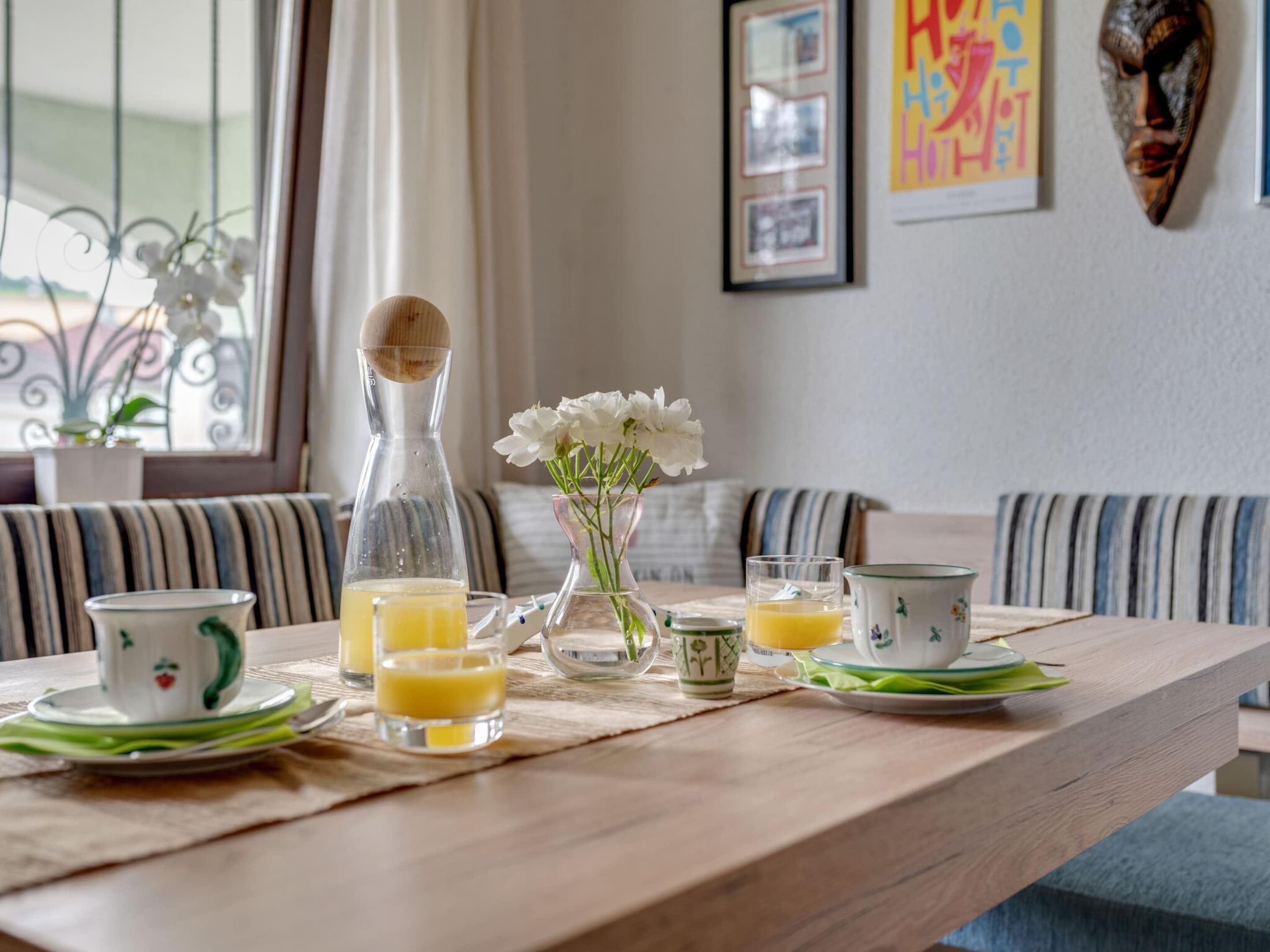 Ett frukostbord med en kanna, en tekanna, koppar och en vas med blommor.
