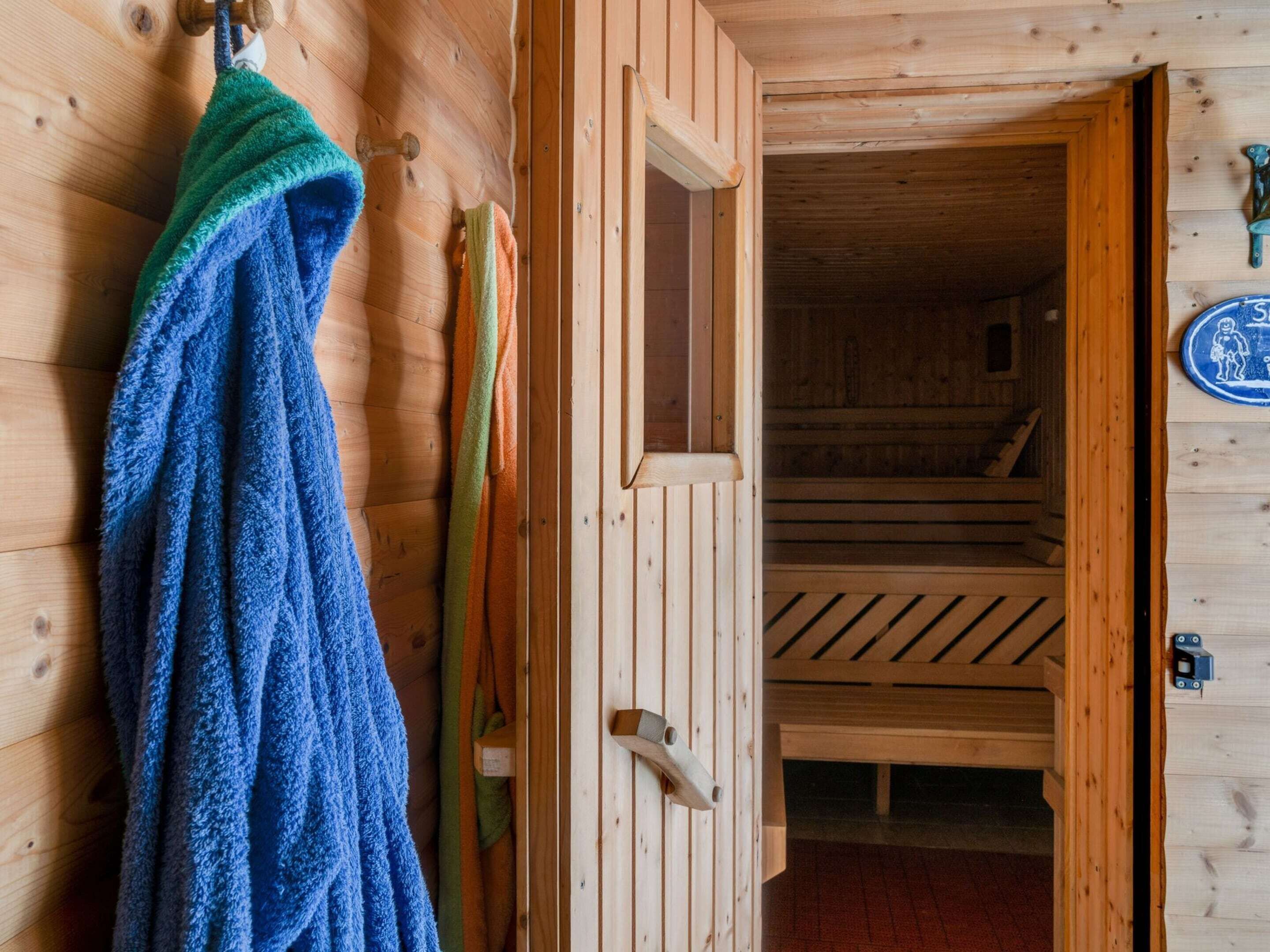 A wooden cabin interior with a wooden door, a towel hanging on the wall, and a bed with a wooden headboard.