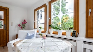 A cozy room with a white sofa, a wooden table with a floral tablecloth, and a window with potted plants. - Alpine Family Retreat in Bad Mitterndorf (Bad Mitterndorf)