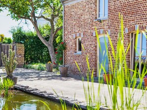 A brick house with a small garden, a pond, and a tree.