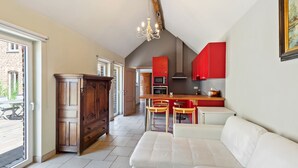 Ein geräumiger Wohnbereich mit einem weißen Sofa, einem Holzkasten und einer Küche mit roten Schränken und einer Pendelleuchte.