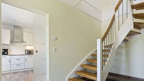 A modern interior with a wooden staircase, a kitchen with white cabinets, and a tiled floor. - Holiday Home in Doberan With Garden (Kuehlungsborn)