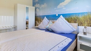 A bedroom with a bed, a wardrobe, a nightstand, and a mural of a beach scene. - Holiday Home in Doberan With Garden (Kuehlungsborn)