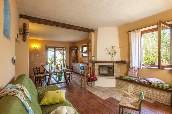 A cozy living room with a fireplace, a dining area, and a kitchen in the background.