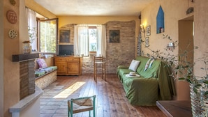 A cozy room with a wooden floor, a green sofa, a wooden cabinet, and a television. - Belvilla by OYO Le Castorelle (Colli al Metauro)