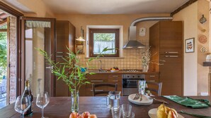 A kitchen with wooden cabinets, a dining table set with wine glasses, apples, and a pitcher. - Belvilla by OYO Le Castorelle (Colli al Metauro)