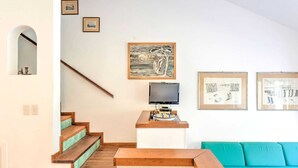 A living room with a staircase, a flat-screen TV, and a teal sofa. - Beachside Holiday Home in Punta Ala (Castiglione della Pescaia)