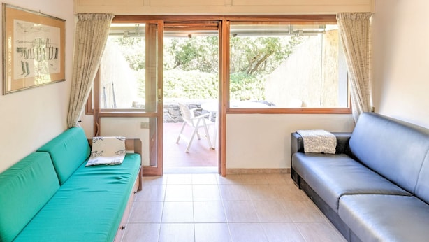 A room with a green sofa, a black sofa, a large window with curtains, and a framed picture on the wall. - Beachside Holiday Home in Punta Ala (Castiglione della Pescaia)