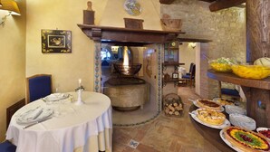 A rustic dining area with a round table set for a meal, a stone fireplace, and a variety of dishes displayed on a shelf. - Holiday Home in Collazone With Pool & Sauna (Collazzone)