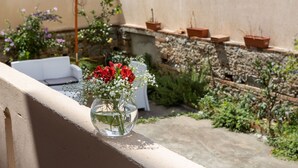 Un balcón con un jarrón de flores rojas y escabiosa blanca, plantas en macetas y un paraguas blanco.