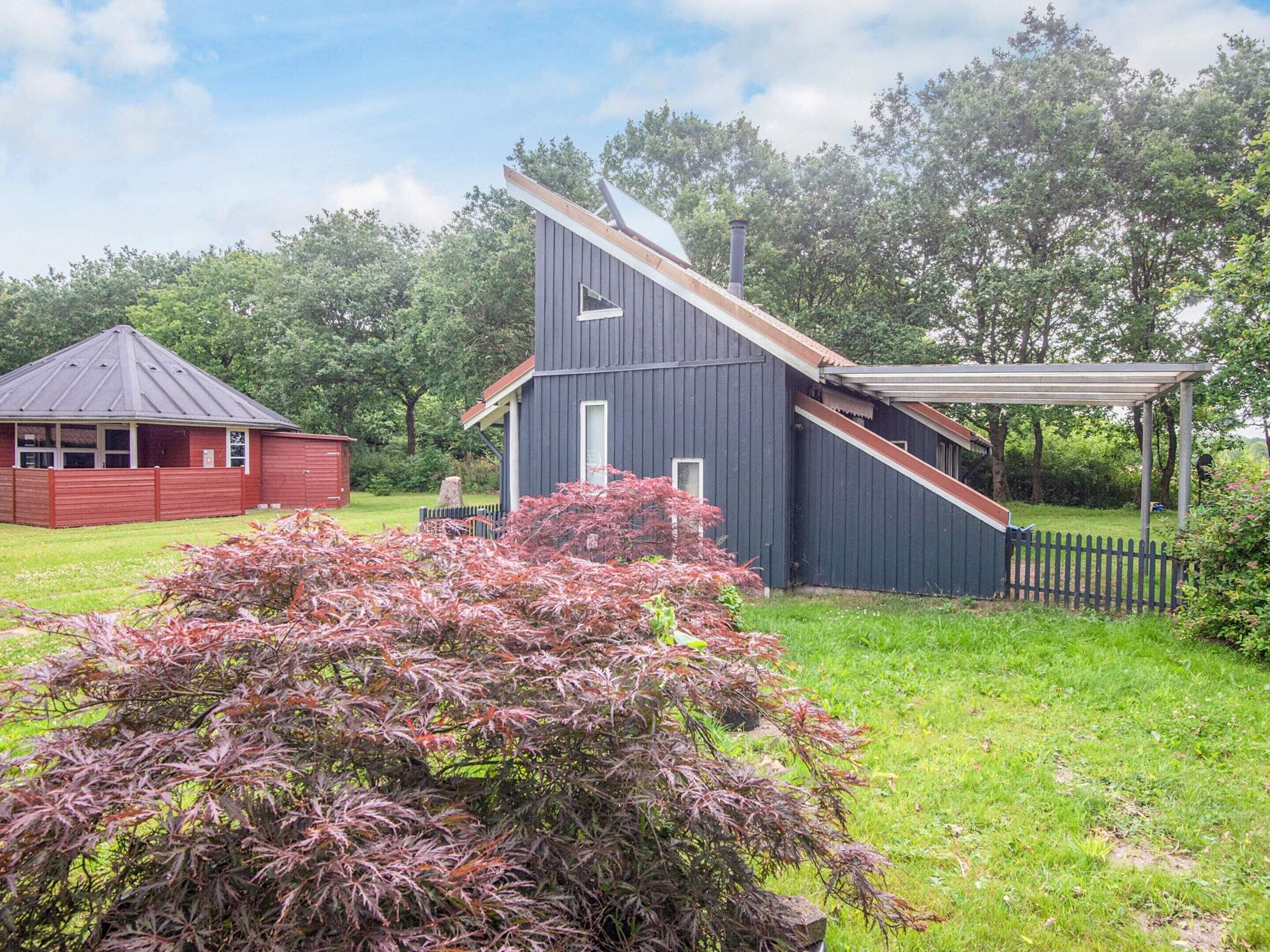 Une maison moderne avec un toit en pente, un porche couvert et un abri de jardin rouge en arrière-plan.