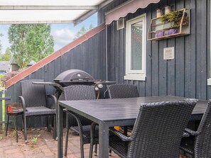 Un patio esterno con una griglia, mobili in vimini e una finestra con uno scaffale sopra.