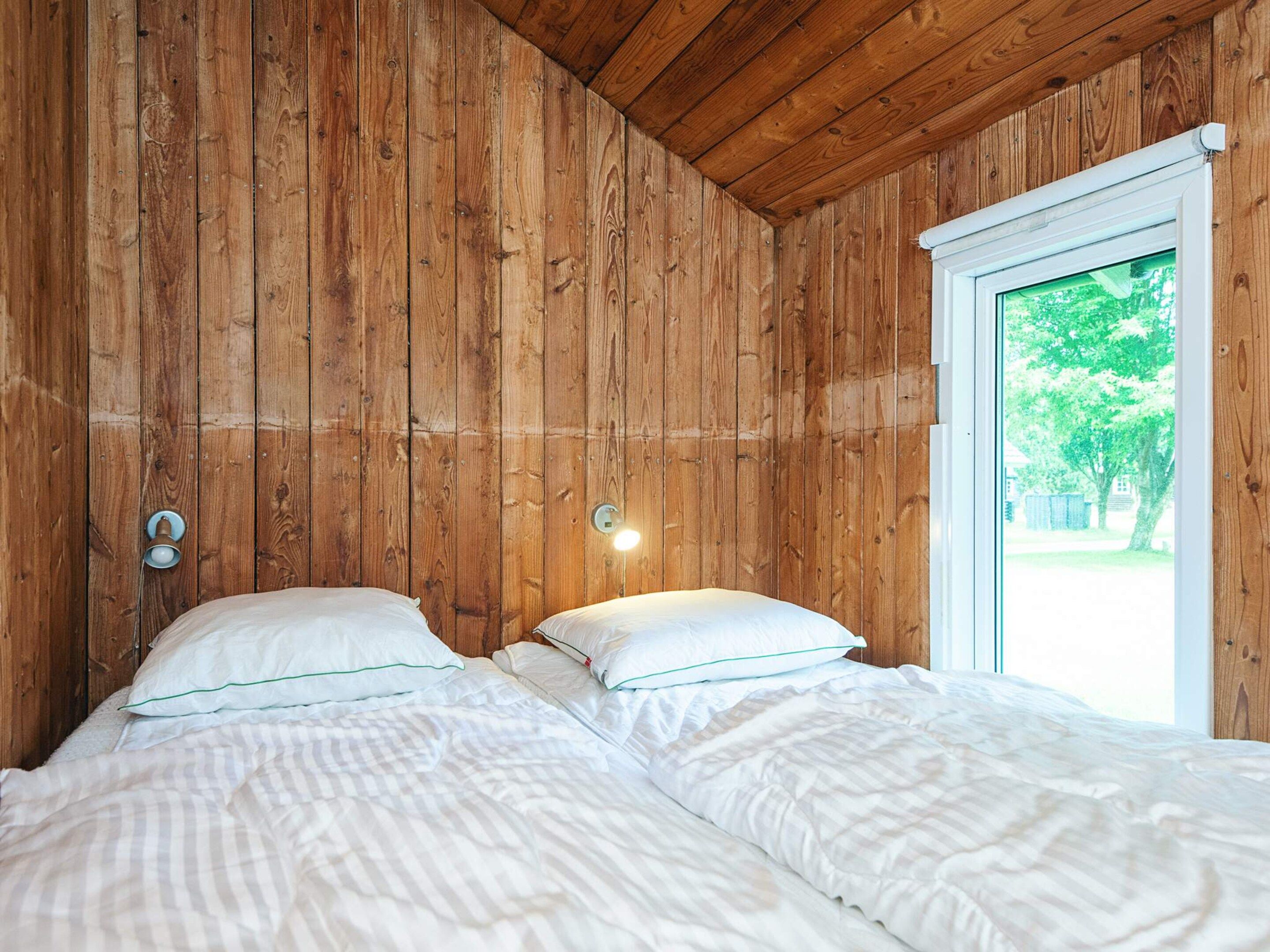 A room with wooden walls, a window, and two beds with white bedding.