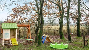 Un parque infantil con columpios, tobogán y estructura para escalar en una zona boscosa.
