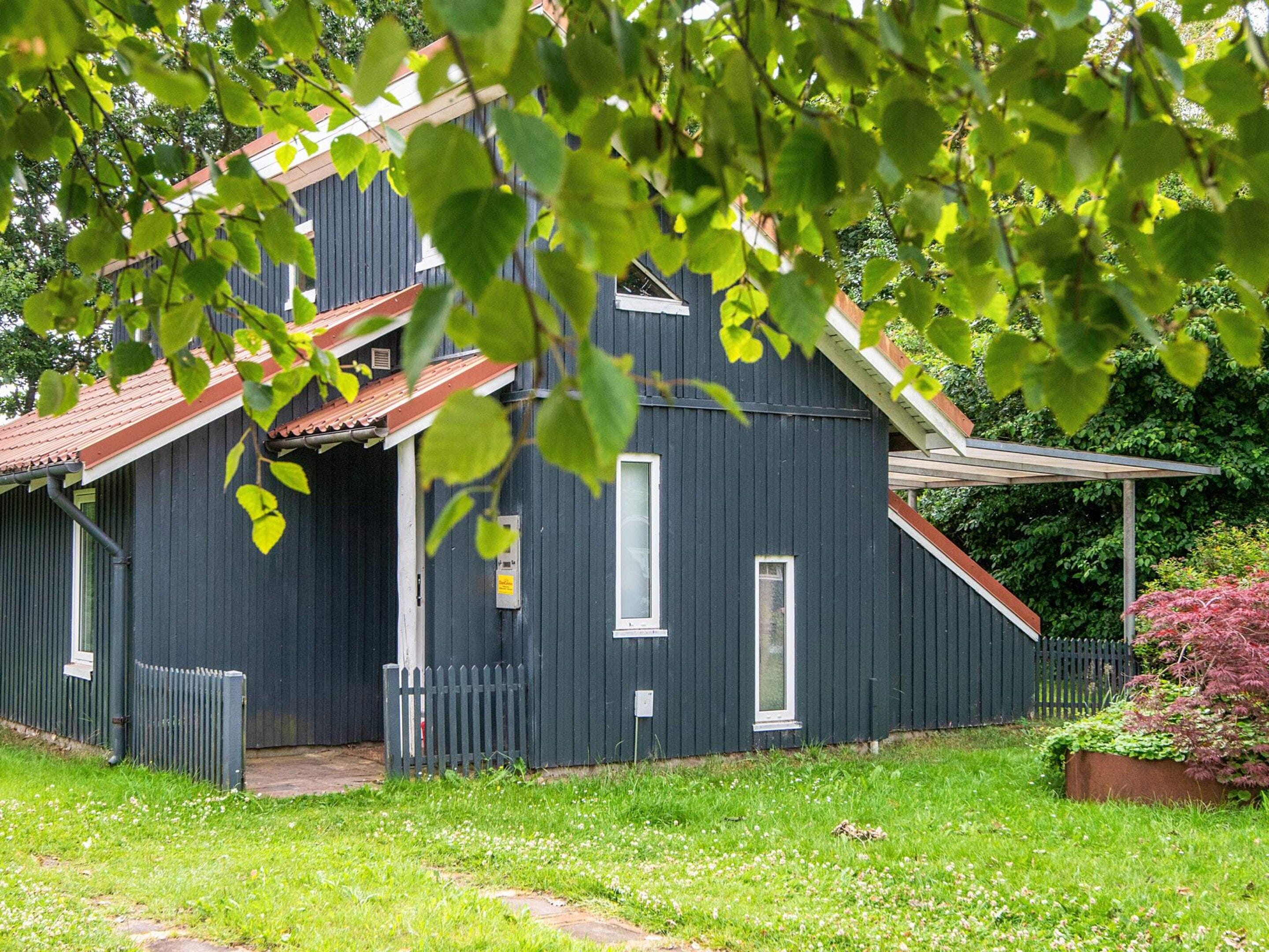 A dark wooden building with a red roof, a small porch, and a fenced yard.