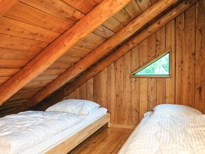 Une pièce aux murs en bois et au plafond en pente, comprenant deux lits avec du linge de lit blanc.