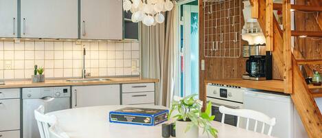 Una cocina con armarios blancos, un lavavajillas Bosch, una mesa de comedor blanca con sillas y una lámpara colgante.