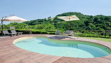 Una piscina con cubierta de madera, sillas de descanso y sombrillas.