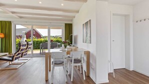 A spacious living area with a dining table, chairs, and a sofa. There is a large window with curtains, a television, and a painting on the wall. - Holiday Home Near the Baltic Sea Beach (Zierow)