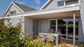 A modern house with a covered patio, a dining area with a table and chairs, and a large sliding glass door leading to a garden. - Holiday Home Near the Baltic Sea Beach (Zierow)