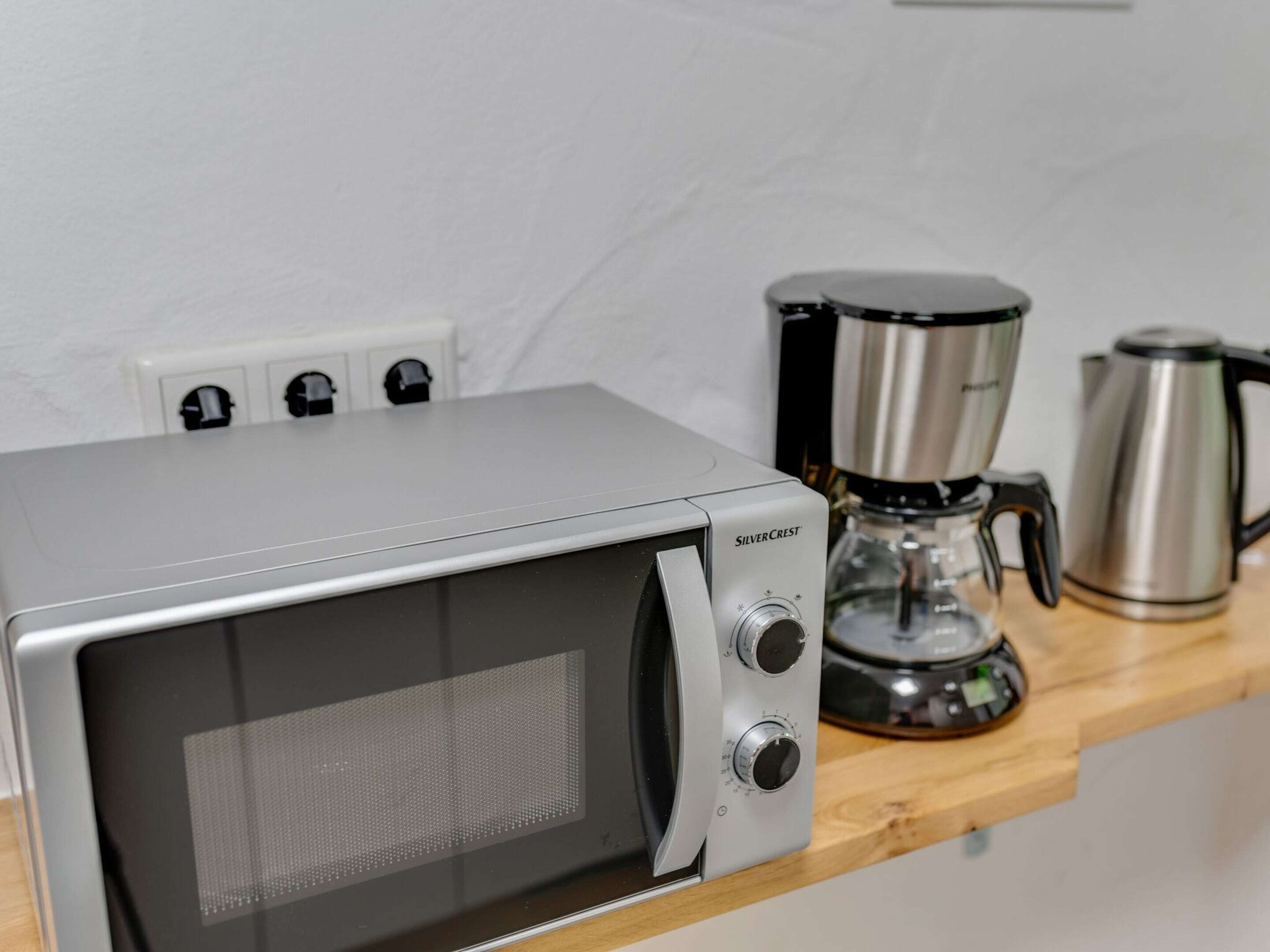 A compact kitchen with a microwave, a coffee maker, and a kettle on a wooden countertop.