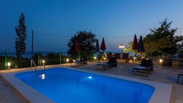 Une piscine entourée d’une clôture et d’arbres, avec des chaises longues et des parasols.